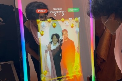 Une femme interagit avec un miroir photobooth lumineux affichant une photo personnalisée d'anniversaire.