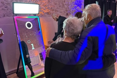 Un couple âgé observe un miroir interactif lumineux dans une salle aux murs en pierre, entouré de plusieurs personnes.