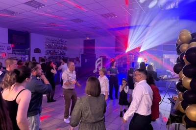 Des personnes dansent et discutent dans une salle éclairée par des lumières colorées, décorée de ballons noirs et dorés.