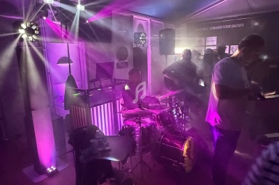 Un batteur joue sur scène dans une ambiance lumineuse violette et tamisée, entouré de spectateurs.