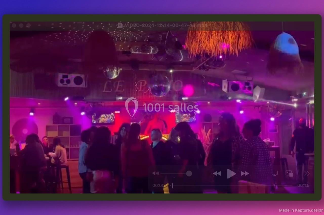 Groupe de personnes dans un bar ou club avec éclairage violet, piste de danse et décorations lumineuses.