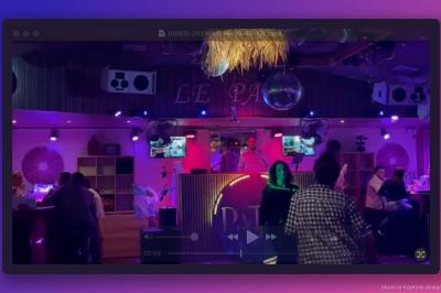 Personnes dansant dans une ambiance festive avec des lumières colorées, vue depuis une table de mixage de DJ.