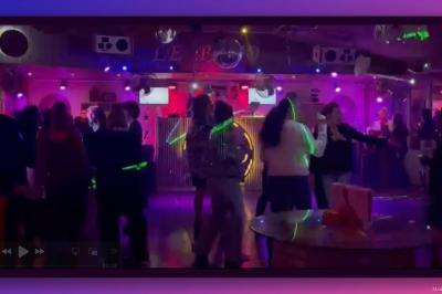 Personnes dansant dans une ambiance festive avec des lumières colorées, vue depuis une table de mixage de DJ.