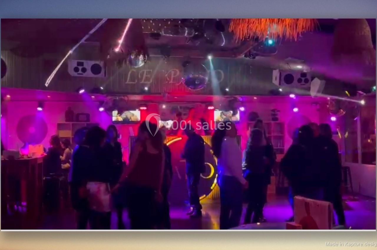 Des personnes dansent dans une salle éclairée par des lumières colorées, avec une ambiance festive et musicale.