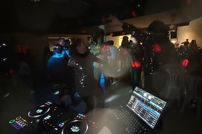 Personnes dansant dans une ambiance festive avec des lumières colorées, vue depuis une table de mixage de DJ.