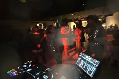Personnes dansant dans une ambiance festive avec des lumières colorées, vue depuis une table de mixage de DJ.