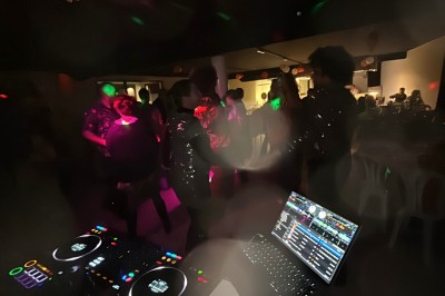 Personnes dansant dans une ambiance festive avec des lumières colorées, vue depuis une table de mixage de DJ.