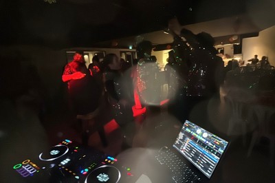 Personnes dansant dans une ambiance festive avec des lumières colorées, vue depuis une table de mixage de DJ.