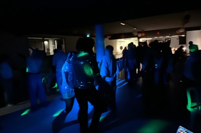 Personnes dansant dans une salle sombre éclairée par des lumières colorées, ambiance festive.