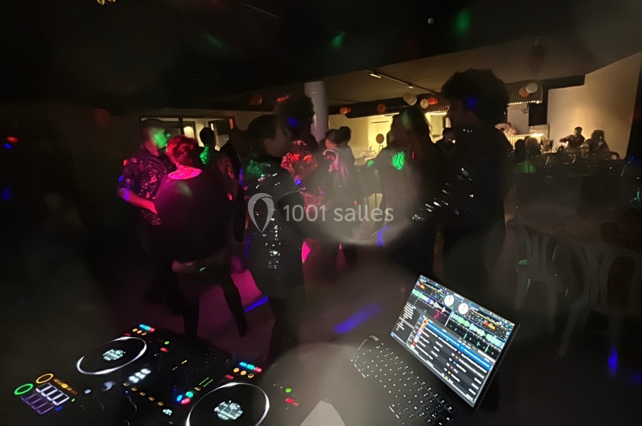 Personnes dansant dans une salle sombre éclairée par des lumières colorées, avec une table de DJ au premier plan.