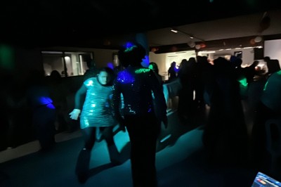 Personnes dansant dans une salle sombre éclairée par des lumières colorées, ambiance festive.