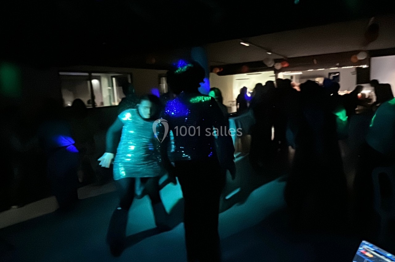 Personnes dansant dans une salle sombre éclairée par des lumières colorées, ambiance festive.