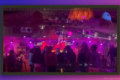 Groupe de personnes dans un bar ou club avec éclairage violet, décorations suspendues et ambiance festive.