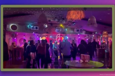 Des personnes dansent dans une salle colorée avec des lumières vives, des décorations suspendues et une ambiance festive.