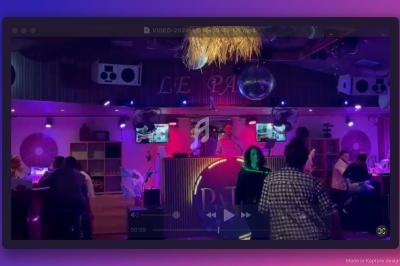 Personnes dansant et socialisant dans un club avec éclairage coloré, un DJ en arrière-plan sur une scène.