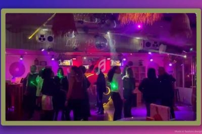 Personnes dansant dans une salle éclairée par des lumières colorées, ambiance festive et conviviale.