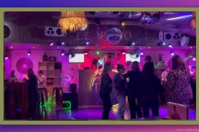 Des personnes dansent devant un DJ dans un bar à l'ambiance lumineuse et colorée.