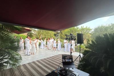 Groupe de personnes en tenue blanche dans un jardin, rassemblées sur une terrasse près d'un équipement de DJ.