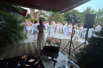 Groupe de personnes habillées en blanc dansant en extérieur près d'une table de mixage et d'enceintes.
