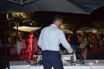 Un DJ mixe de la musique lors d'une fête en plein air, avec des invités dansant sous des lumières colorées.