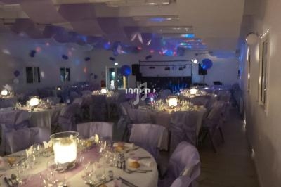 Salle de réception décorée avec des nappes et chaises violettes, tables dressées et éclairage tamisé.