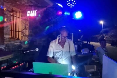 Un DJ mixant en extérieur de nuit, entouré de lumières colorées et d'équipements audio.