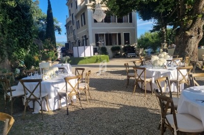 Tables de réception dressées en extérieur sur une terrasse en gravier, entourées de verdure et d'un bâtiment élégant.