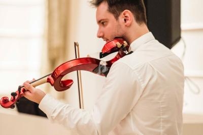 Un homme joue du violon rouge dans une pièce lumineuse avec un haut-parleur en arrière-plan.