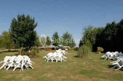 Chaises blanches empilées et disposées sur une pelouse entourée d'arbres par une journée ensoleillée.