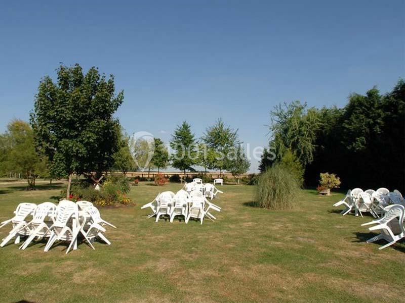 Chaises blanches empilées et disposées sur une pelouse entourée d'arbres par une journée ensoleillée.