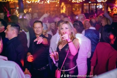 Des personnes dansent et discutent dans une ambiance festive avec des lumières colorées en arrière-plan.