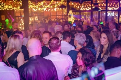 Foule rassemblée dans un lieu festif éclairé par des guirlandes lumineuses et une ambiance colorée.