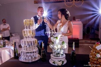 Un couple de mariés trinque devant une pièce montée, un gâteau de mariage et une fontaine de champagne.