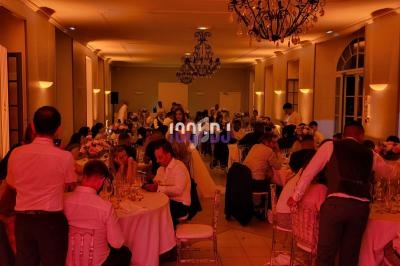 Salle de réception illuminée, avec des invités assis à des tables rondes lors d'un événement festif.