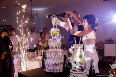 Un couple de mariés remplit une pyramide de coupes de champagne lors d'une réception, entouré d'invités.