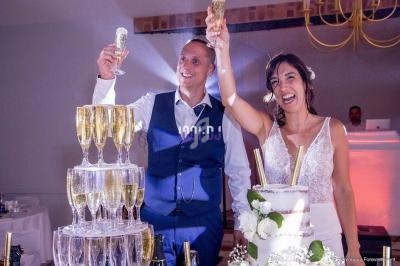 Un couple souriant lève des coupes de champagne près d'une pièce montée lors d'une célébration.