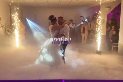 Un couple danse au milieu d'une piste enveloppée de fumée, entouré de jets d'étincelles et d'invités en arrière-plan.