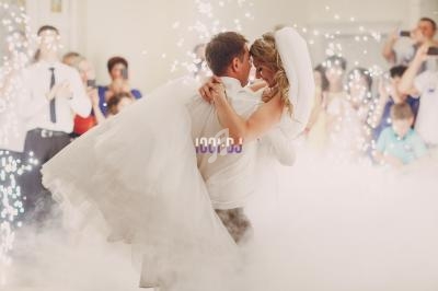 Un couple de mariés danse au milieu de la fumée et des étincelles, entouré d'invités qui les observent.