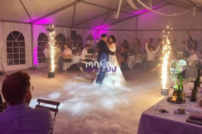 Un couple danse au centre d'une salle décorée, entouré de fumée et d'effets pyrotechniques, sous le regard des invités.