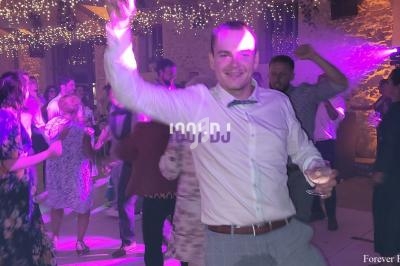 Un homme souriant danse sous des lumières colorées lors d'une soirée festive avec des invités en arrière-plan.
