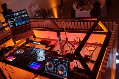 Poste de DJ avec platines, table de mixage, ordinateur portable et tablette, éclairé par des lumières colorées.