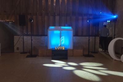 Scène de mariage avec une piste de danse éclairée, une décoration ’LOVE’ lumineuse et des projecteurs bleus.