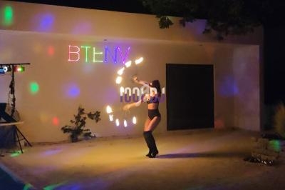 Personne jonglant avec des bâtons lumineux dans une cour éclairée par des lumières colorées, de nuit.