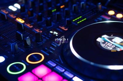 Table de mixage DJ avec platines, boutons lumineux et pads rétroéclairés dans un environnement sombre.