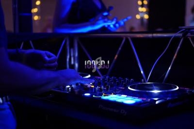 Un DJ manipule une table de mixage lumineuse dans une ambiance sombre avec des lumières bleues.