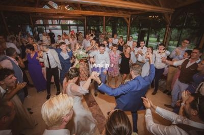 Des invités dansent en cercle autour des mariés dans une salle avec de grandes fenêtres donnant sur un espace vert.