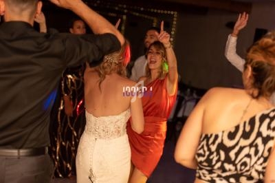 Des personnes dansent lors d'une fête, une femme en robe orange lève le bras en souriant.