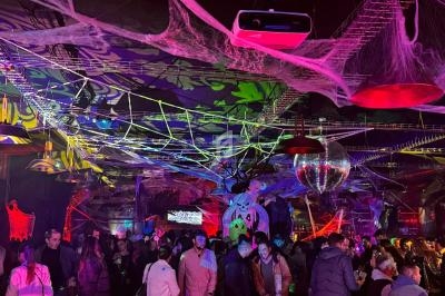 Salle décorée pour Halloween avec toiles d'araignée, éclairages colorés et foule rassemblée lors d'une soirée festive.