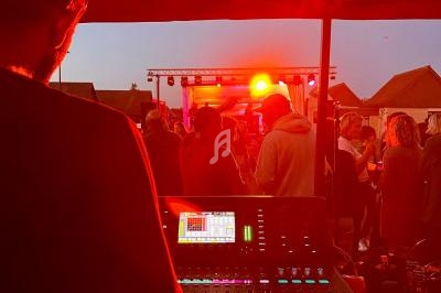 Technicien son ajustant une console de mixage lors d'un concert en plein air éclairé par des lumières rouges.