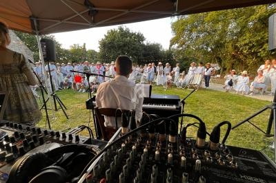 Un musicien joue du piano en plein air devant un public, avec une console audio au premier plan.